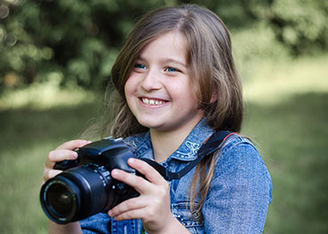 Das Bild zeigt ein lachendes Mädchen mit einer Fotokamera